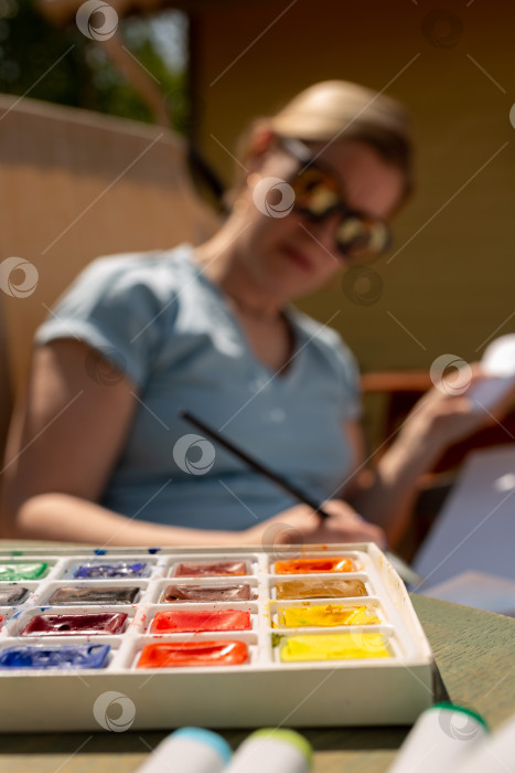 Скачать Акварельные краски на столе на фоне художника, который рисует в альбоме для рисования фотосток Ozero