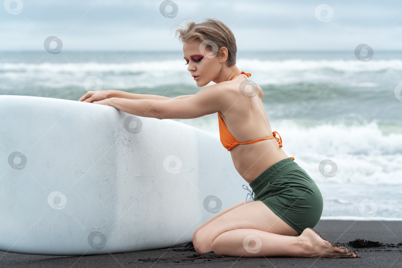 Скачать Женщина-серфер с закрытыми глазами стоит на коленях и держит свою доску для серфинга во время летних каникул фотосток Ozero