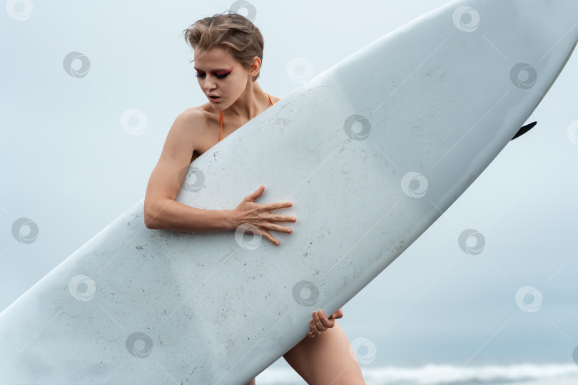 Скачать Крупный план женщины-спортивной фотомодели, держащей в руках белую доску для серфинга и стоящей за ней фотосток Ozero