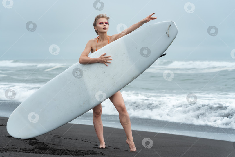 Скачать Женщина с доской для серфинга в руках и поразительной расслабленной позой, которая просто кричит о летних каникулах фотосток Ozero
