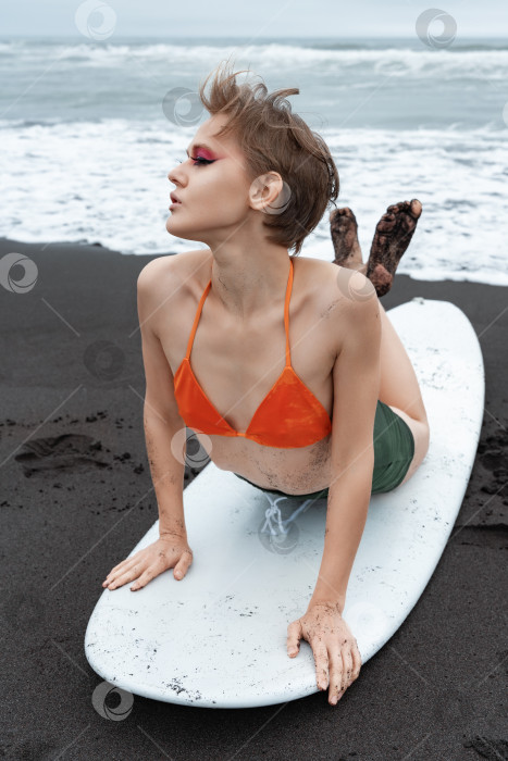 Скачать Женщина-серфер, лежащая на доске для серфинга, выполняет разминочное упражнение перед тренировкой во время летнего пляжного отдыха фотосток Ozero