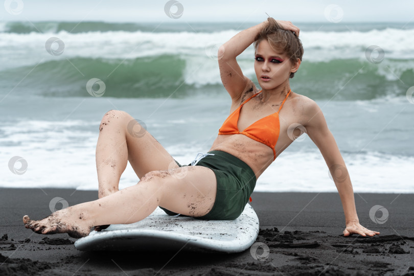 Скачать Женщина-серфер сидит на доске для серфинга, она выглядит такой аутентичной и неподдельной, и даже смотрит в камеру фотосток Ozero
