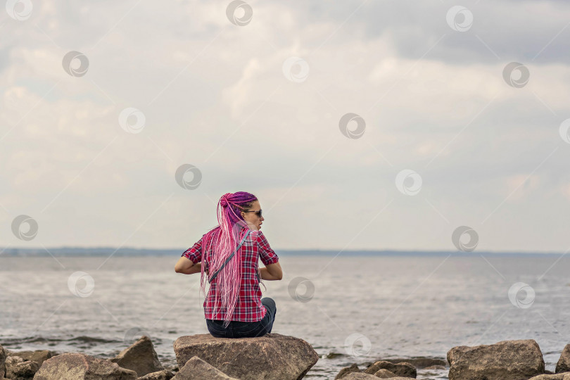 Скачать Молодая женщина с розовыми волосами сидит на камнях на берегу моря. Финский залив фотосток Ozero