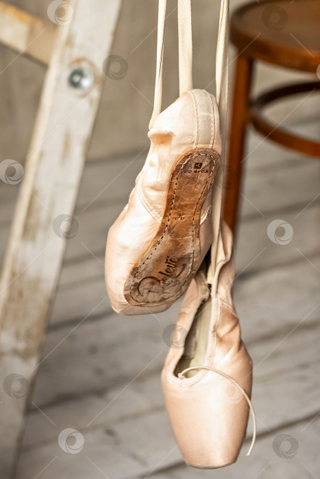 Скачать Балетные туфли висят на перекладине в танцевальном зале. Концепция танца, балетная школа, обувь для балерин. Новые пуанты с подвешенными к ним атласными лентами. фотосток Ozero