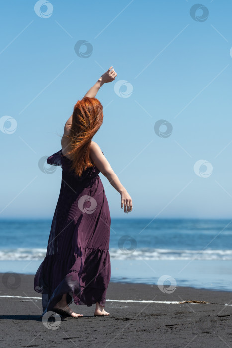 Скачать Женщина, стоящая на пляже, на фоне кристально синего моря. Она выглядит такой элегантной в длинном платье фотосток Ozero