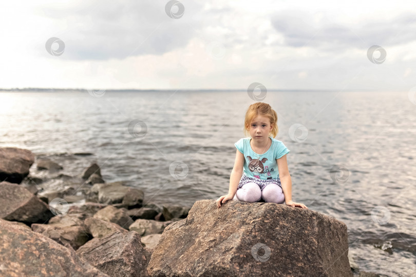 Скачать Маленькая девочка сидит на камнях у моря. Финский залив. Летнее время фотосток Ozero