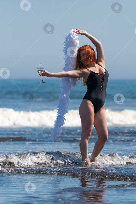 Скачать Удивительная женщина, стоящая в морских волнах, с бокалом вина в одной руке и боа в другой фотосток Ozero