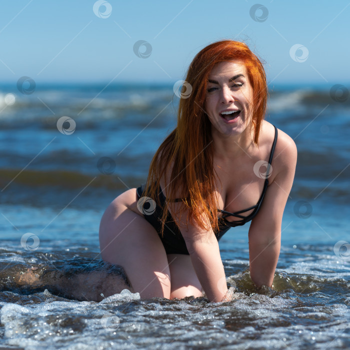 Скачать Восторженная женщина в купальнике видна стоящей на коленях в разбивающихся о берег волнах прибоя во время пляжного отдыха фотосток Ozero