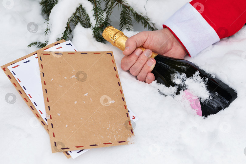 Скачать Рождественские письма и рука Санта-Клауса с бутылкой шампанского на снегу, концепция на тему плохого Санты, теряющего детские письма фотосток Ozero