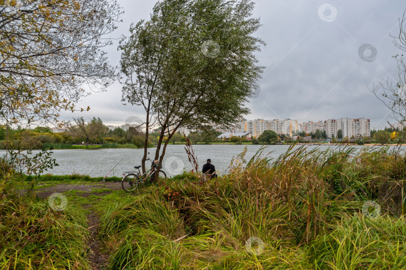 Скачать Рыбак на берегу ловит рыбу в городском пруду фотосток Ozero