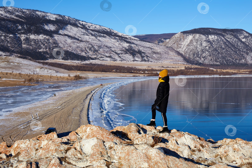 Скачать Молодая девушка путешествует по озеру Байкал зимой. Красивый зимний горный пейзаж, прозрачный лед фотосток Ozero