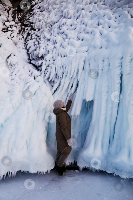 Скачать Женщина любуется огромными сосульками и глыбами льда и снега на скалах. Зимнее путешествие по озеру Байкал. фотосток Ozero