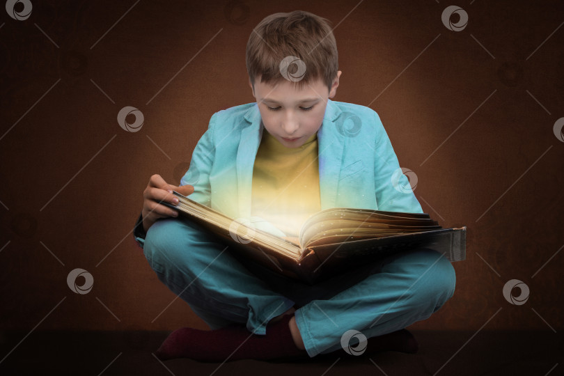 Скачать Мальчик читает книгу, излучающую волшебное сияние. фотосток Ozero