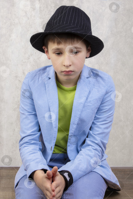 Скачать Грустный стильный мальчик в элегантной шляпе и синем костюме задумчив. фотосток Ozero