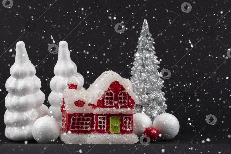 Скачать Праздничный снежный темный рождественский фон. Красный миниатюрный домик, окруженный белыми рождественскими елками. фотосток Ozero