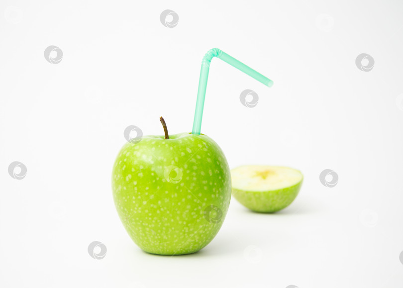 Скачать Зеленое яблоко на белом фоне, в него вставлена трубочка для коктейля, половина яблока лежит на заднем плане. фотосток Ozero