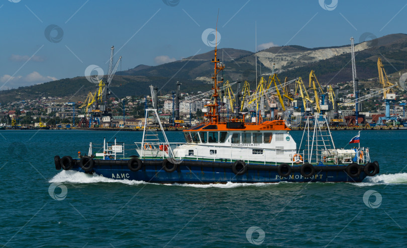 Скачать Морской лоцман "Адис" плывет по голубым водам Черного моря. Белое рабочее судно "Адис" в Новороссийском морском торговом порту на фоне Кавказских гор.  Новороссийск, Россия - 15 сентября 2021 г. фотосток Ozero