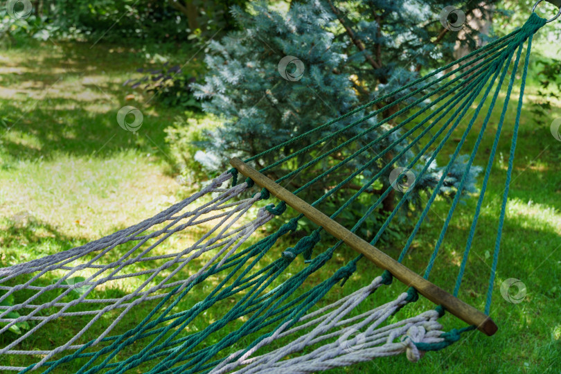Скачать Фрагмент плетеного веревочного гамака в фокусе на размытом фоне красивого зеленого летнего сада. Атмосфера предстоящих каникул. Яркий солнечный день фотосток Ozero