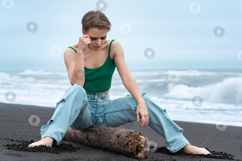 Скачать Женщина, сидящая на бревне с раздвинутыми ногами и опущенной головой, смотрит вниз на пляж Тихого океана фотосток Ozero