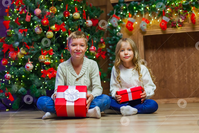 Скачать Семья в канун Рождества у камина. Дети открывают рождественские подарки. Дети под рождественской елкой с подарочными коробками. Оформленная гостиная с традиционным камином. Уютный теплый зимний вечер дома. фотосток Ozero