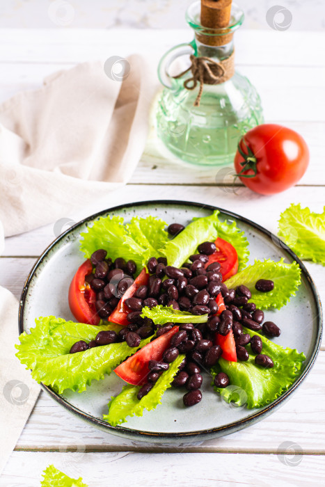 Скачать Вегетарианский салат из черной фасоли, помидоров и листьев салата-латука на тарелке вертикальный вид фотосток Ozero