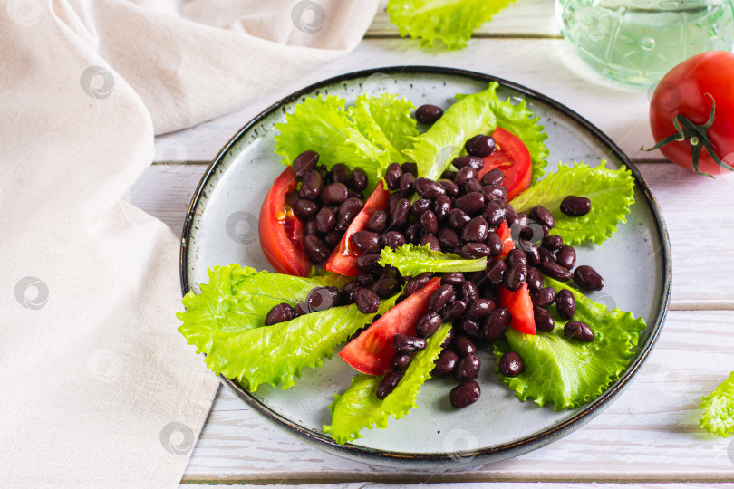 Скачать Вегетарианский салат из черной фасоли, помидоров и листьев салата-латука на тарелке фотосток Ozero