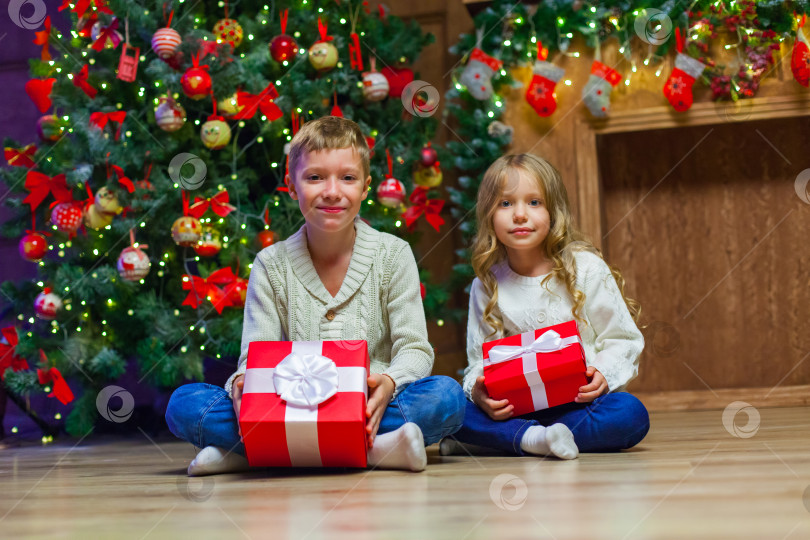 Скачать Семья в канун Рождества у камина. Дети открывают рождественские подарки. Дети под рождественской елкой с подарочными коробками. Оформленная гостиная с традиционным камином. Уютный теплый зимний вечер дома. фотосток Ozero