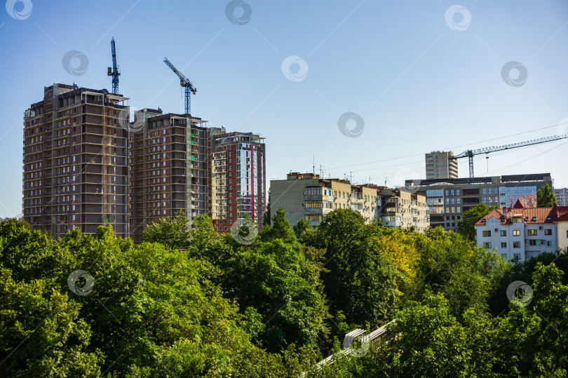 Скачать Вид из окна на строительство многоэтажного жилого дома. Центр города. Парковая зона на переднем плане. Строительные краны над небоскребами. фотосток Ozero