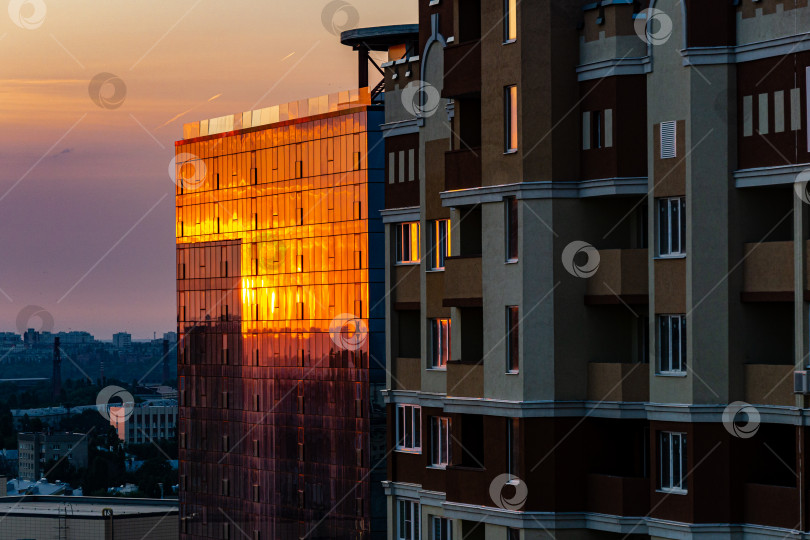 Скачать Высотное здание крупным планом на фоне заката. Солнечные лучи оранжевым цветом отражаются в стеклянных окнах высотного здания. фотосток Ozero