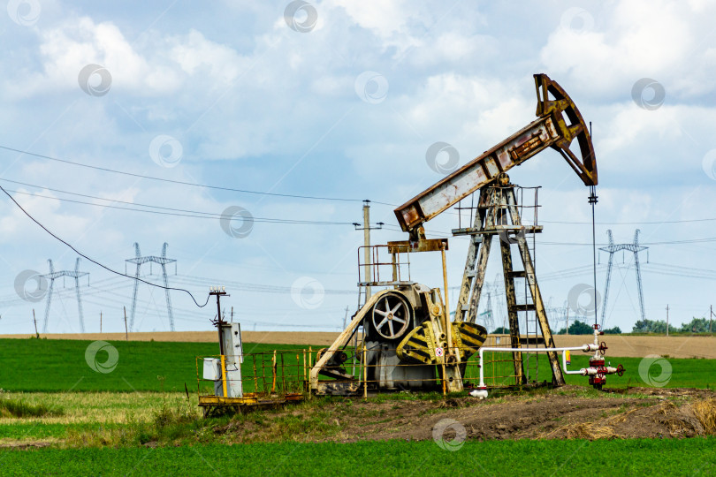 Скачать Нефтяная вышка качает нефть на фоне желтого поля и пасмурного неба. фотосток Ozero