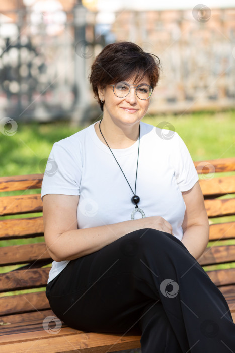 Скачать Красивая женщина средних лет в очках и с короткими темными волосами сидит на скамейке фотосток Ozero