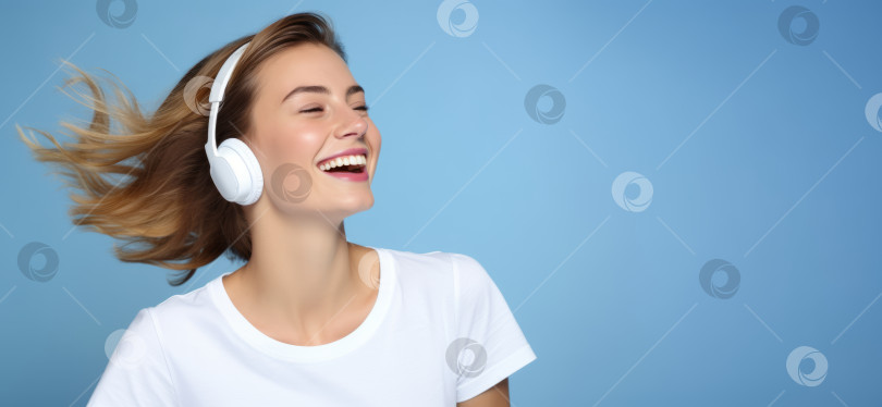 Скачать Счастливая, смеющаяся молодая женщина в белой футболке и наушниках на светло-голубом фоне с пробелом для копирования фотосток Ozero