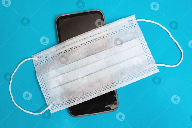 Скачать Мобильный телефон в медицинской маске на синем фоне фотосток Ozero