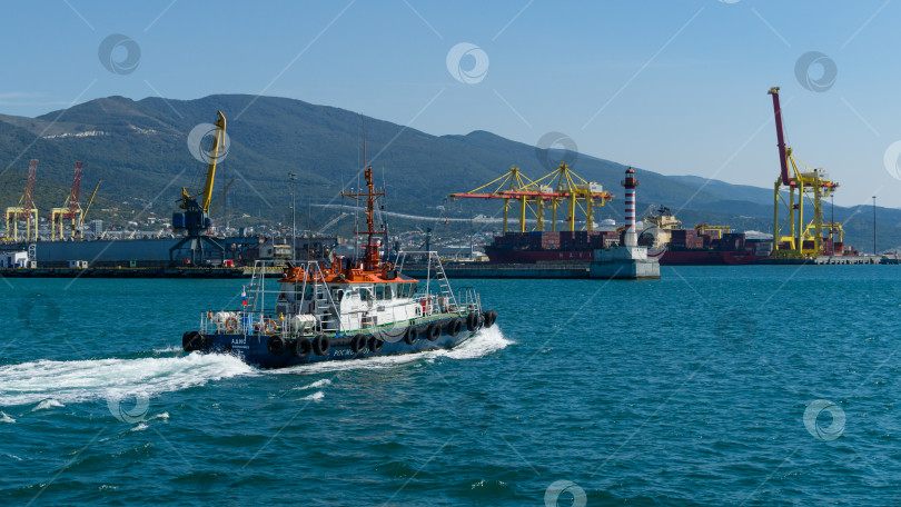 Скачать Морской лоцман "Адис" плывет по бирюзовой воде вдоль Цемесского залива. Крупный план белого рабочего катера "Адис" на фоне Новороссийского морского торгового порта.  Новороссийск, Россия - 15 сентября 2021 г. фотосток Ozero