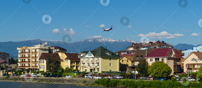 Скачать Boeing 737-8LJ (WL) совершает посадку над зданиями на побережье горной реки Мзымта на фоне вершин Кавказских гор. Федеральная территория Сириус в Имеретинской низменности. Адлер Сириус, Россия - 18 мая 2021 г. фотосток Ozero