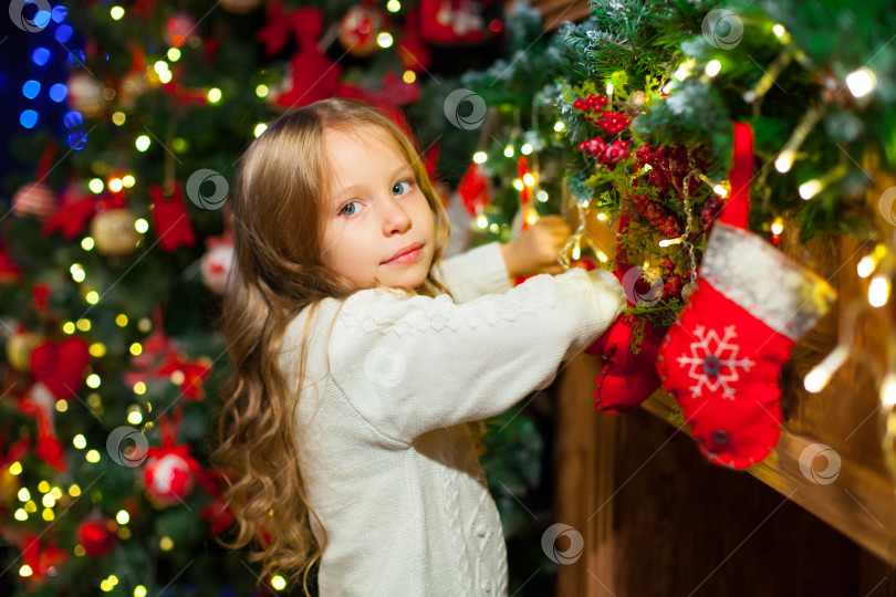 Скачать Симпатичная девочка-малышка проверяет свой рождественский чулок под красивой елкой фотосток Ozero