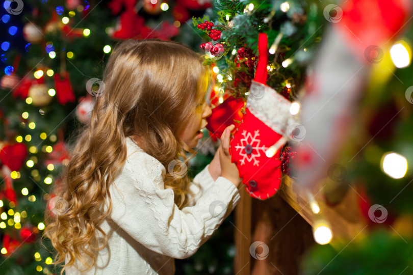 Скачать Симпатичная девочка-малышка проверяет свой рождественский чулок под красивой елкой фотосток Ozero