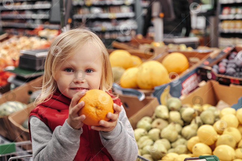 Скачать Маленькая девочка сидит в корзине для покупок в продуктовом магазине или супермаркете фотосток Ozero