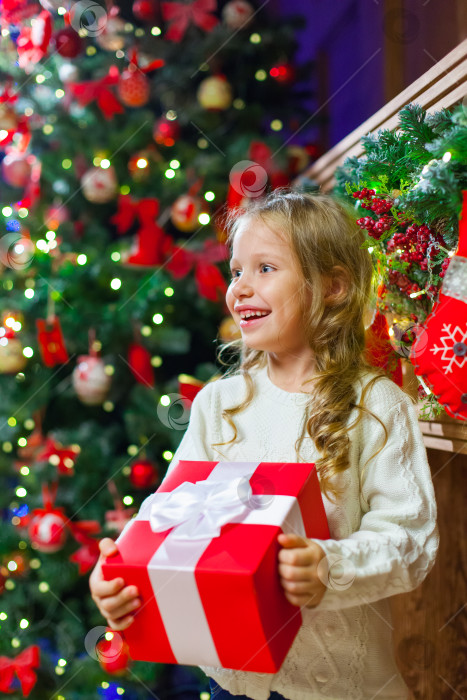 Скачать Маленькая девочка сидит у елки с рождественским подарком в руках очень весело смеется фотосток Ozero