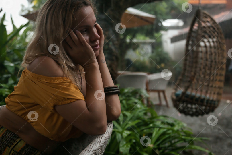 Скачать Молодая женщина грустит под тропическим дождем, глубоко задумавшись и переживая фотосток Ozero
