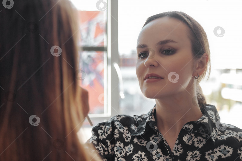 Скачать Женщина-визажист делает макияж симпатичной молодой женщине в салоне красоты фотосток Ozero