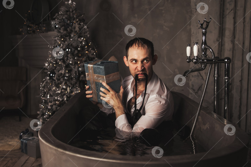 Скачать Депрессивный сумасшедший мужчина с подарочной рождественской коробкой в отделе психического здоровья в ванне в ванной комнате фотосток Ozero