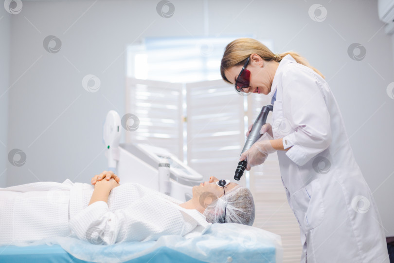 Скачать Снимок лица молодой девушки в защитных очках с видом сбоку во время процедуры карбонового пилинга в салоне красоты фотосток Ozero