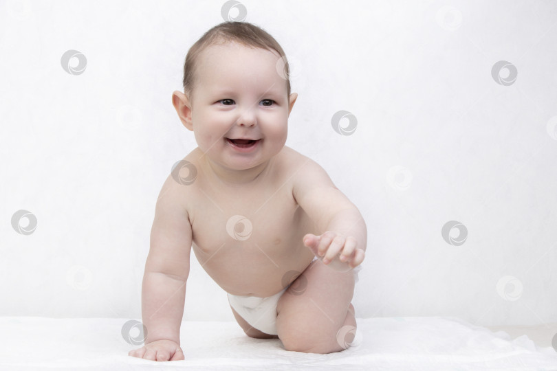 Скачать Малыш с улыбкой на белом фоне. Счастливый шестимесячный мальчик ползает по кровати и смеется. Концептуальная фотография отцовства и материнства. фотосток Ozero