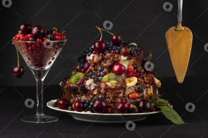 Скачать Роскошный ягодный торт, золотистая лопаточка и стеклянный бокал с красными ягодами на темном фоне. фотосток Ozero