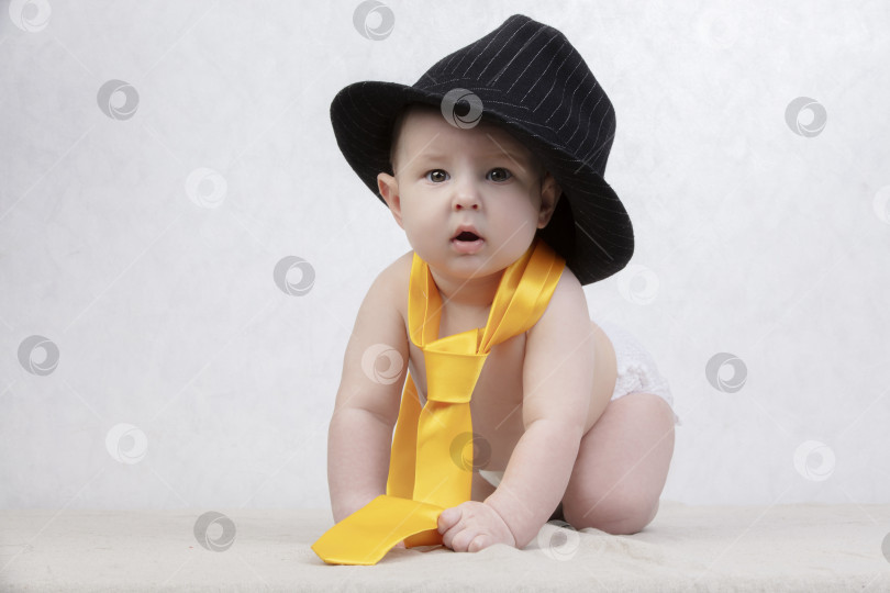 Скачать Улыбающийся малыш в ретро-шляпе и галстуке на белом фоне. Забавный шестимесячный малыш в элегантной одежде. фотосток Ozero