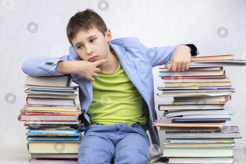 Скачать Грустный задумчивый мальчик-студент сидит между стопками книг. Приобретайте знания. Усталый студент. фотосток Ozero