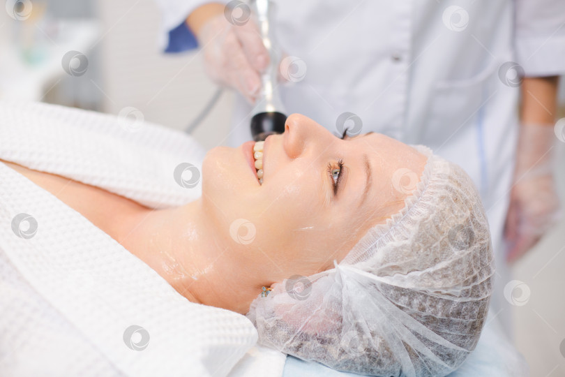 Скачать Крупным планом портрет красивой улыбающейся женщины, отдыхающей во время процедуры RF-лифтинга в современном салоне красоты фотосток Ozero