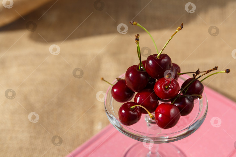 Скачать Натюрморт и фотография с едой. Сервировочная тарелка на ножках и мини-купол с вишневыми ягодами стоят на книге и мешковине фотосток Ozero