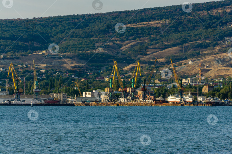 Скачать Вид морского порта в городе на фоне Крымских гор. Портовые краны и корабли вдоль береговой линии. На переднем плане изумрудная вода Черного моря. фотосток Ozero